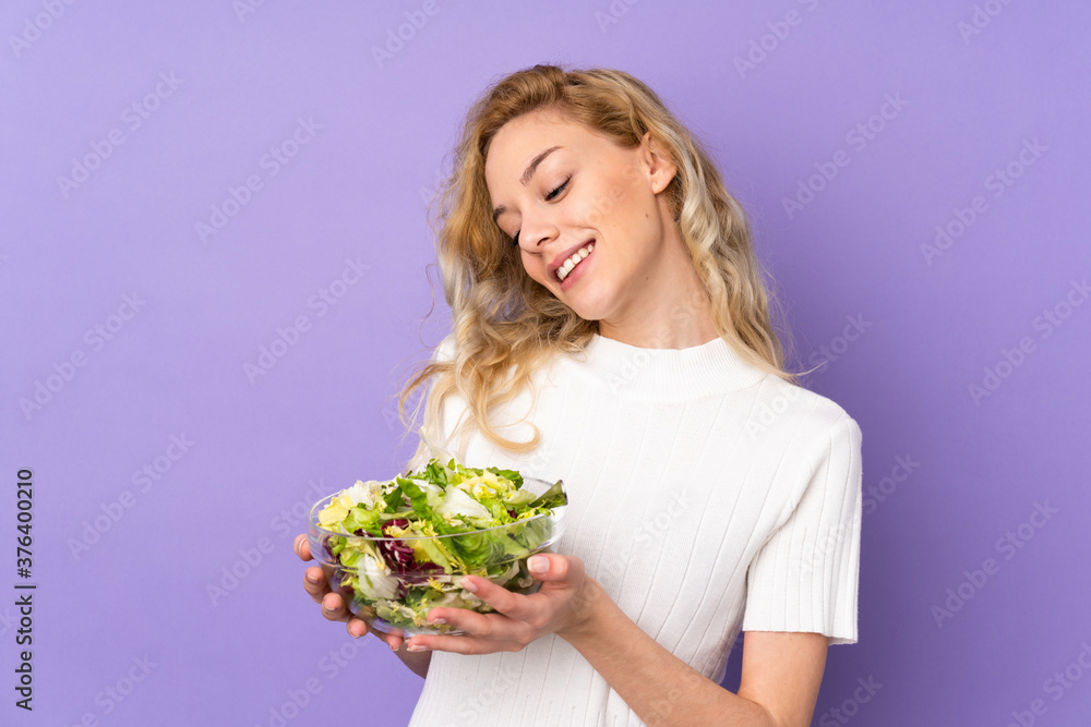 Young blonde woman holding salad isolated on purple background