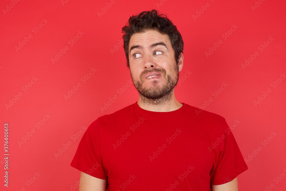 Amazed Young handsome caucasian man wearing t-shirt over isolated red background bitting lip and looking up to empty space, Amazed Young handsome caucasian man wearing t-shirt over isolated red background bitting lip and looking up to empty space,