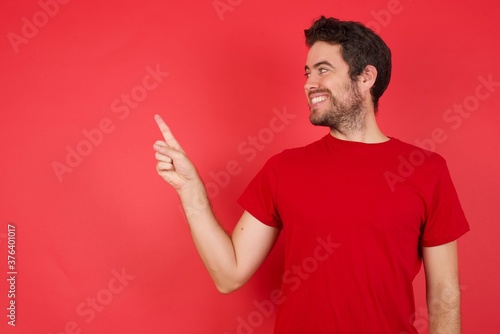 Smiling Young handsome caucasian man wearing t-shirt over isolated red background pointing up and looking at the camera