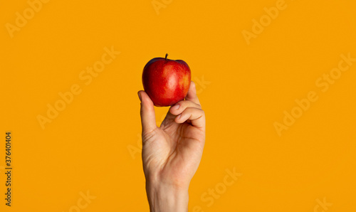 Male hand showing yummy red apple on orange background