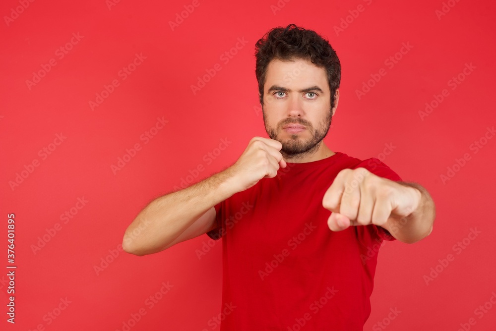 Young handsome caucasian man wearing t-shirt over isolated red background Punching fist to fight, aggressive and angry attack, threat and violence Young handsome caucasian man wearing t-shirt over isolated red background Punching fist to fight, aggressive and angry attack, threat and violence