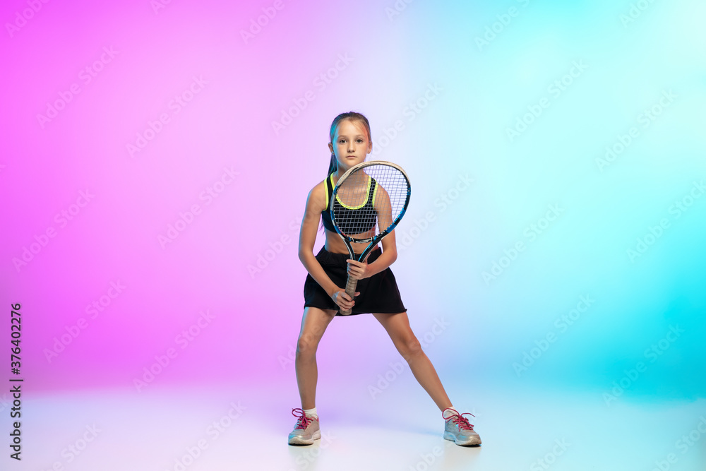 Aspiration. Little tennis girl in black sportwear isolated on gradient background in neon light. Little caucasian model, sport kid training in motion and action. Sport, movement, childhood concept.