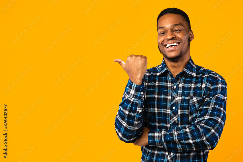 Black Man Pointing Thumb Aside Posing Over Yellow Studio Background Black Man Pointing Thumb Aside Posing Over Yellow Studio Background