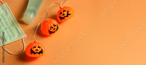 Halloween pumpkin lights, medical mask and alcohol sanitizer gel on orange background. Halloween , COVID-19 prevention and new normal concept.
