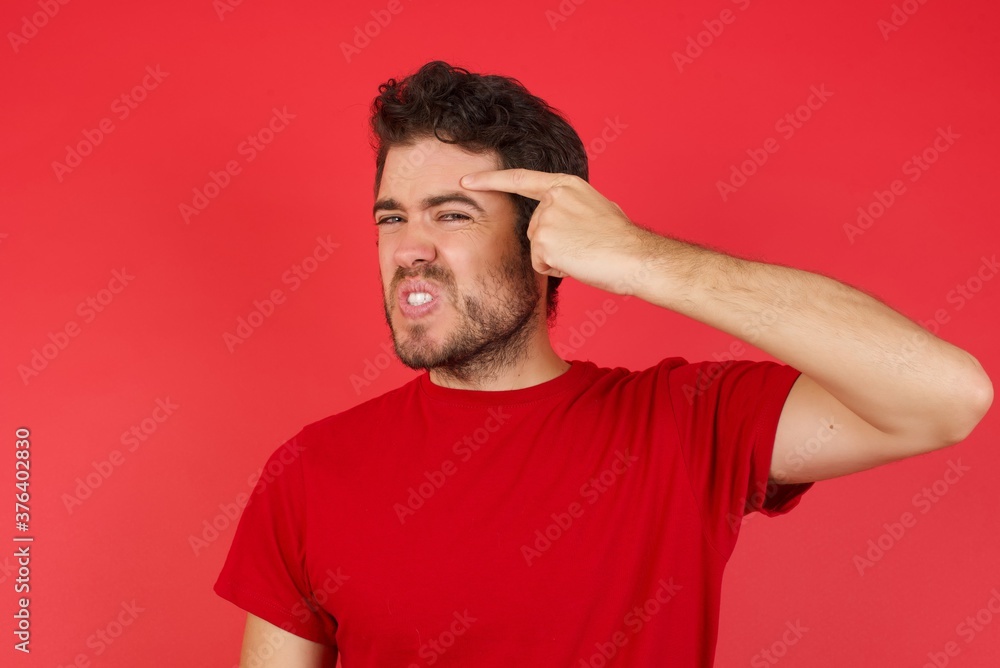 Young handsome caucasian man wearing t-shirt over isolated red background pointing unhappy at pimple on forehead, blackhead infection. Skincare concept. Young handsome caucasian man wearing t-shirt over isolated red background pointing unhappy at pimple on forehead, blackhead infection. Skincare concept.