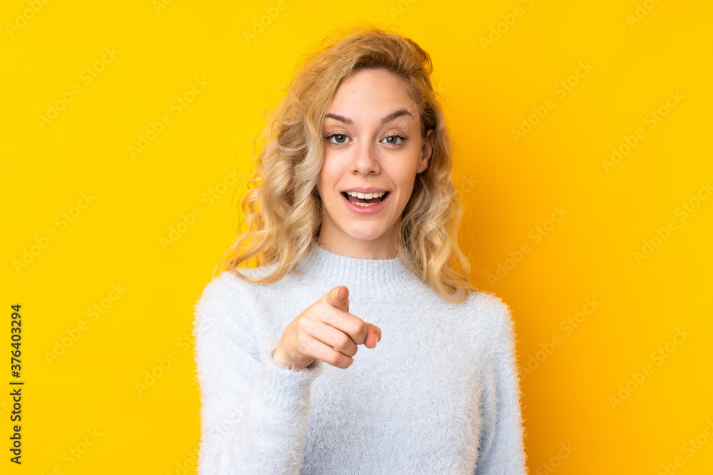 Young blonde woman isolated on yellow background surprised and pointing front Young blonde woman isolated on yellow background surprised and pointing front
