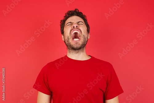 Fotobehang Young handsome caucasian man wearing t-shirt over isolated red background angry and mad screaming frustrated and furious, shouting with anger