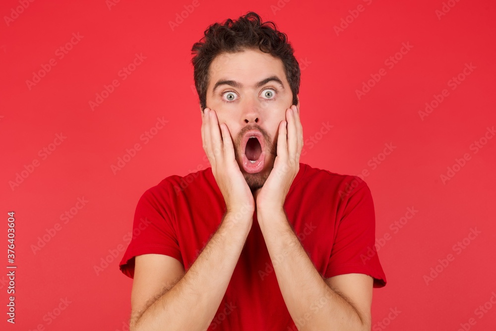 Scared terrified Young handsome caucasian man wearing t-shirt over isolated red wall shocked with prices at shop, being short of money to buy something, People and human emotions concept Scared terrified Young handsome caucasian man wearing t-shirt over isolated red wall shocked with prices at shop, being short of money to buy something, People and human emotions concept