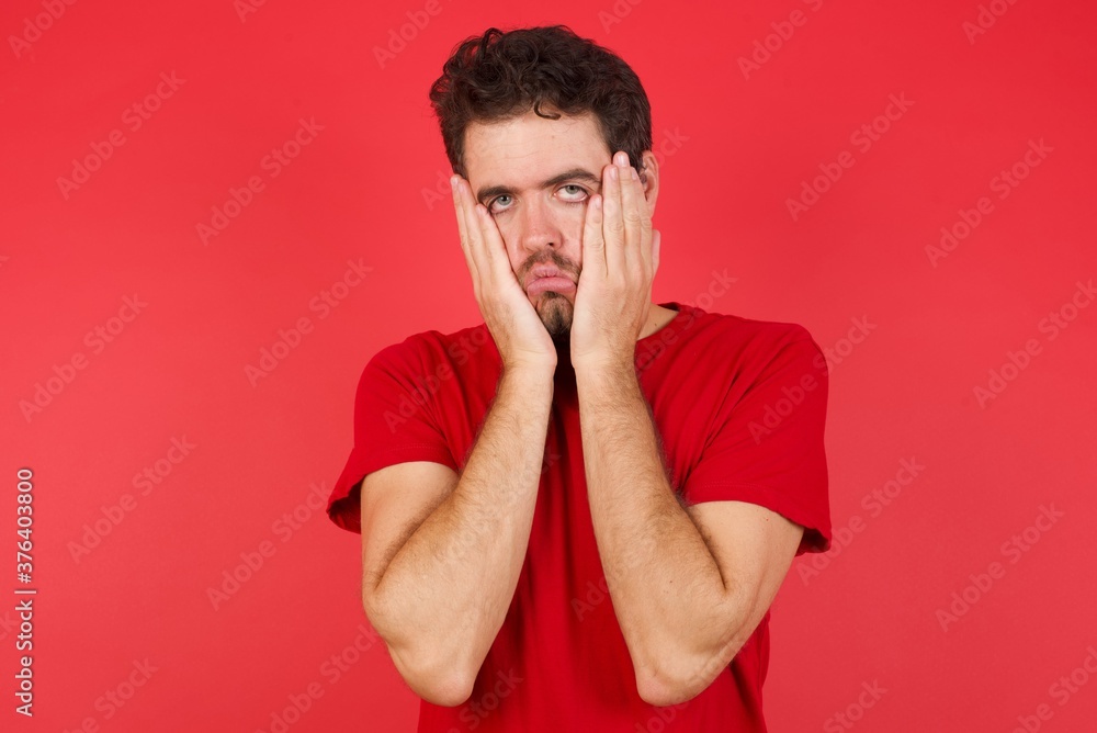 Young handsome caucasian man wearing t-shirt over isolated red background Tired hands covering face, depression and sadness, upset and irritated for problem Young handsome caucasian man wearing t-shirt over isolated red background Tired hands covering face, depression and sadness, upset and irritated for problem