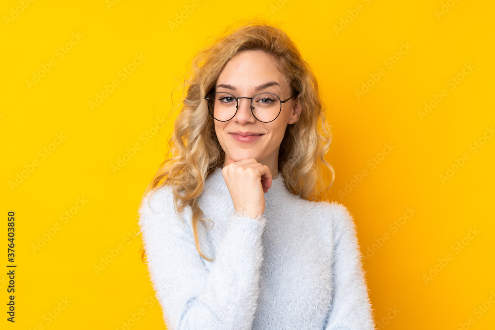 Young blonde woman isolated on yellow background with glasses and smiling