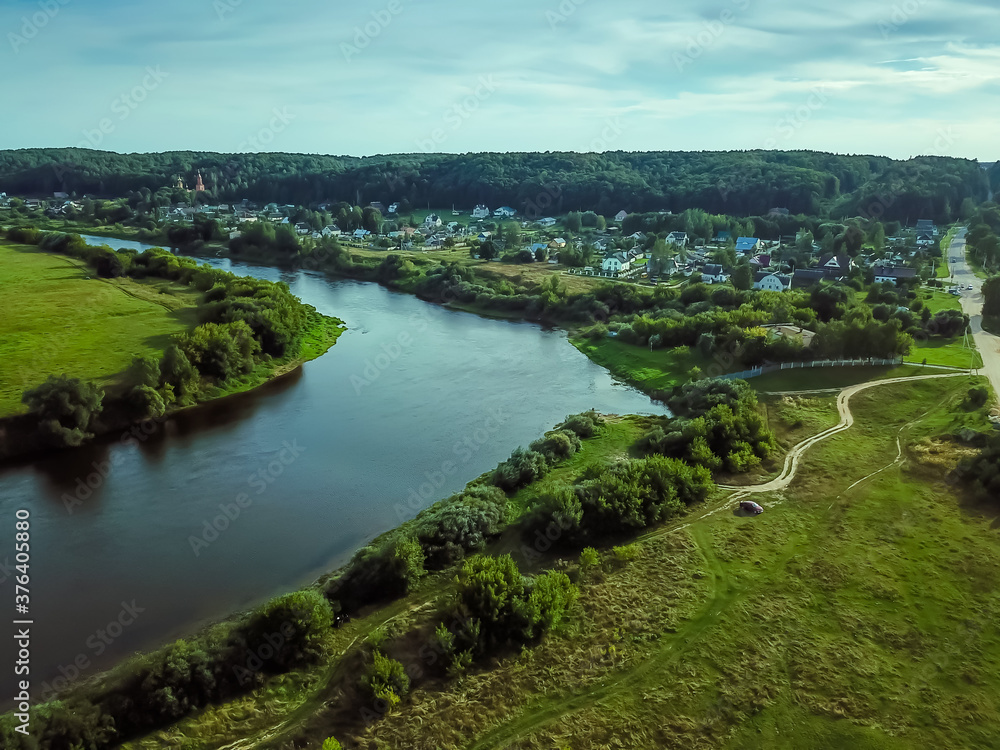 Village near the river, forests during the summer sunset, panoramic view from above by aerial drone