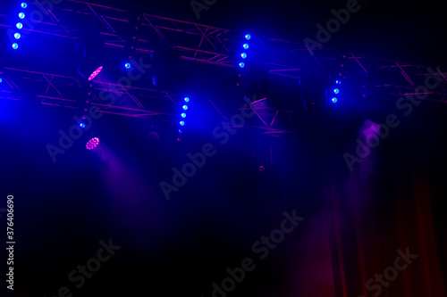 Stage lights. Several projectors in dark. A bright colored spotlight permeates the darkness. Light from the stage, rock concert. Lighting equipment. Several projectors on theatrical lighting system