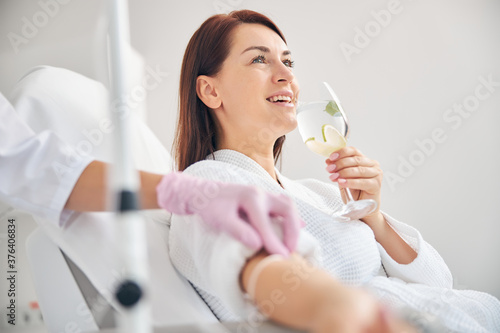 Attractive dark-haired woman smiling during the intravenous therapy