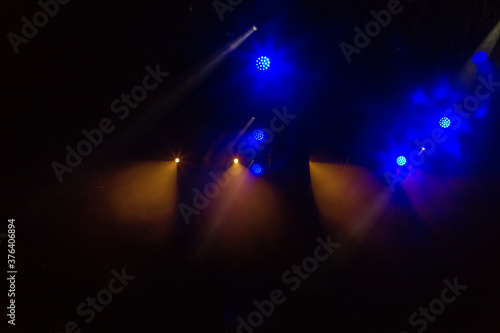 Stage lights. Several projectors in dark. A bright colored spotlight permeates the darkness. Light from the stage, rock concert. Lighting equipment. Several projectors on theatrical lighting system