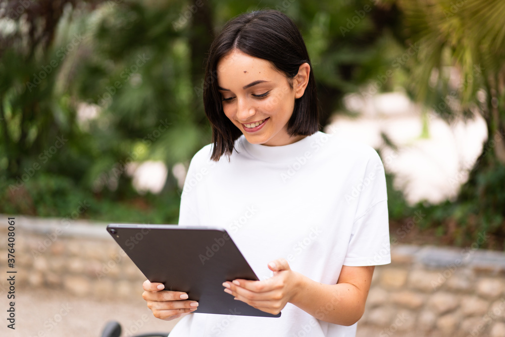 Fototapeta premium Young caucasian woman holding a tablet at outdoors