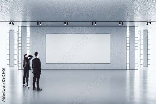 Businessman and businesswoman looking on empty banner on wall.