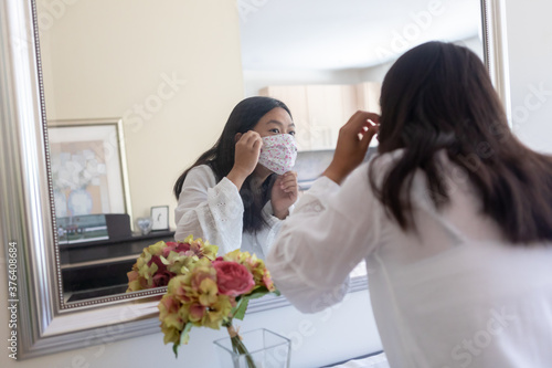 Young Generation Z Asian Woman Putting on COVID Mask Looking in Mirror