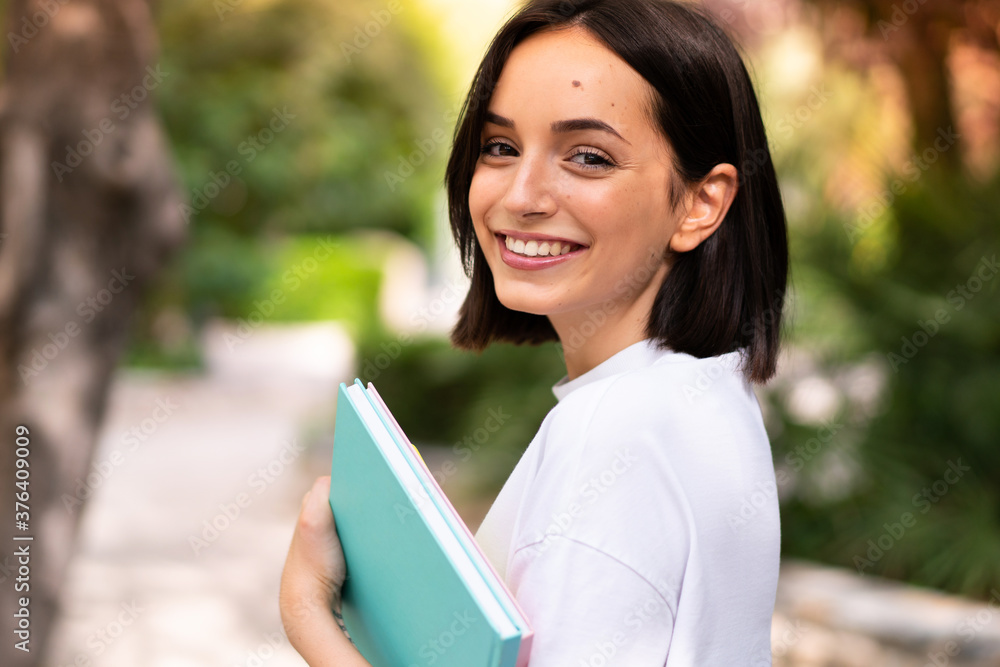 Fototapeta premium Young happy student woman holding notebooks at outdoors