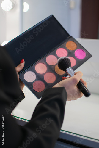 Girl holding professional makeup eyeshadow palette and brush in her hands close-up. Stylist. vertical photo. beauty saloon