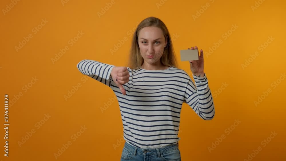 Young woman showing blank gray card, showing thumbs down gesture. The concept of bad shopping, substandard product. Yellow background. 4K video. Young woman showing blank gray card, showing thumbs down gesture. The concept of bad shopping, substandard product. Yellow background. 4K video.