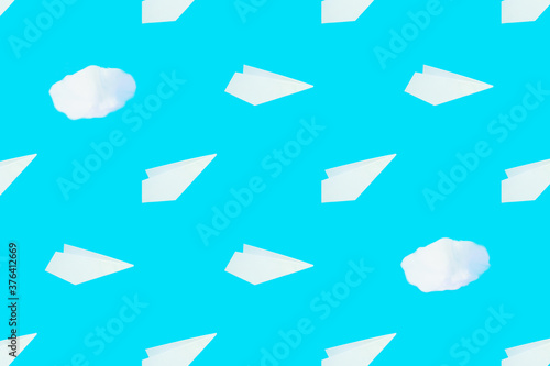 Pattern from white paper airplanes and cotton clouds on a blue background. Creative concept of travel, flights..