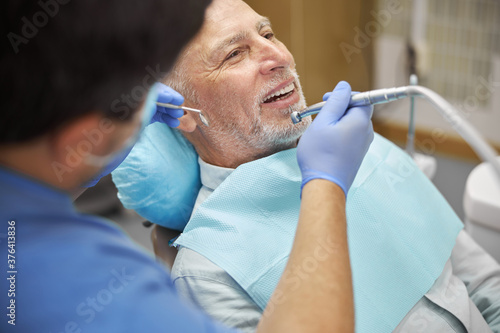 Gladsome aged man having his teeth treated at dental clinic photo