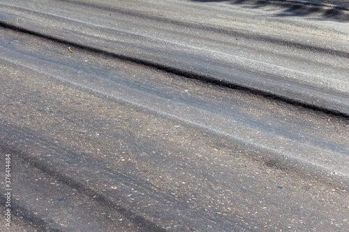 Damaged road  damaged chopped asphalt with potholes and spot. Very bad asphalt road with large trenche. Terrible technology of asphalt production in construction of road. Soft Asphalt melts from heat