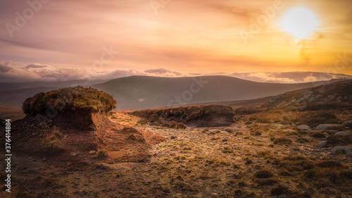 Island of old cut turf or peat, highlighted by setting sun in beautiful scenery of Wicklow mountains. Dramatic sunset and cloudscape at golden hour