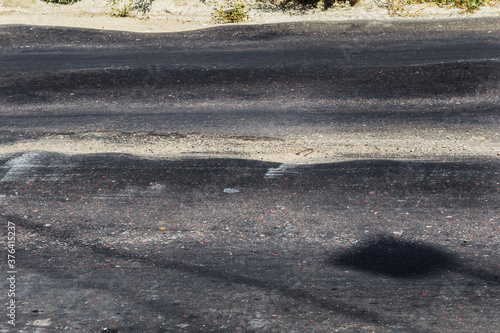 Damaged road, damaged chopped asphalt with potholes and spot. Very bad asphalt road with large trenche. Terrible technology of asphalt production in construction of road. Soft Asphalt melts from heat photo