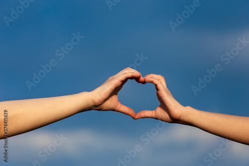 Girl hands in heart form over blue sky background