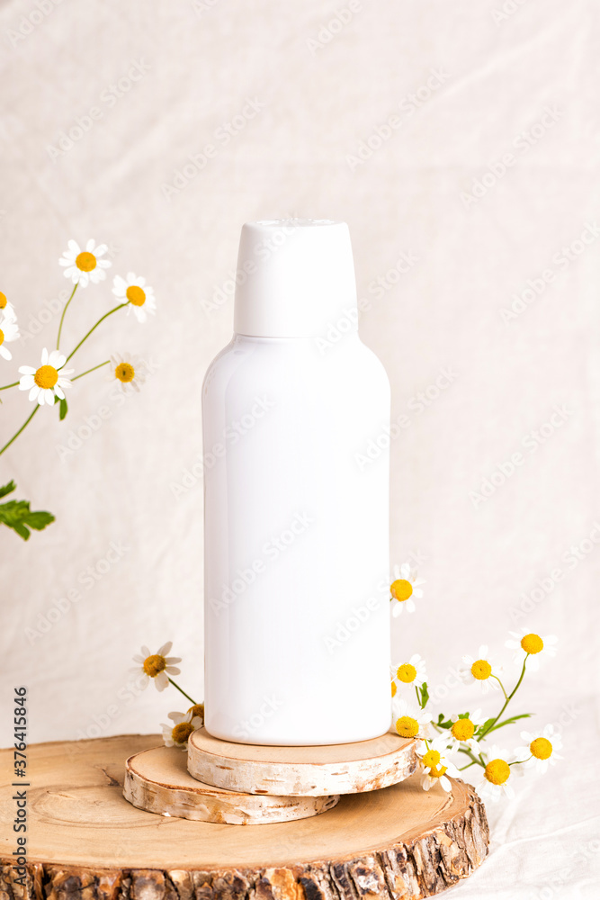Bottle of Mockup cosmetic products with chamomile flowers. Shampoo or mouthwash on wood slice. Beige fabric background Bottle of Mockup cosmetic products with chamomile flowers. Shampoo or mouthwash on wood slice. Beige fabric background