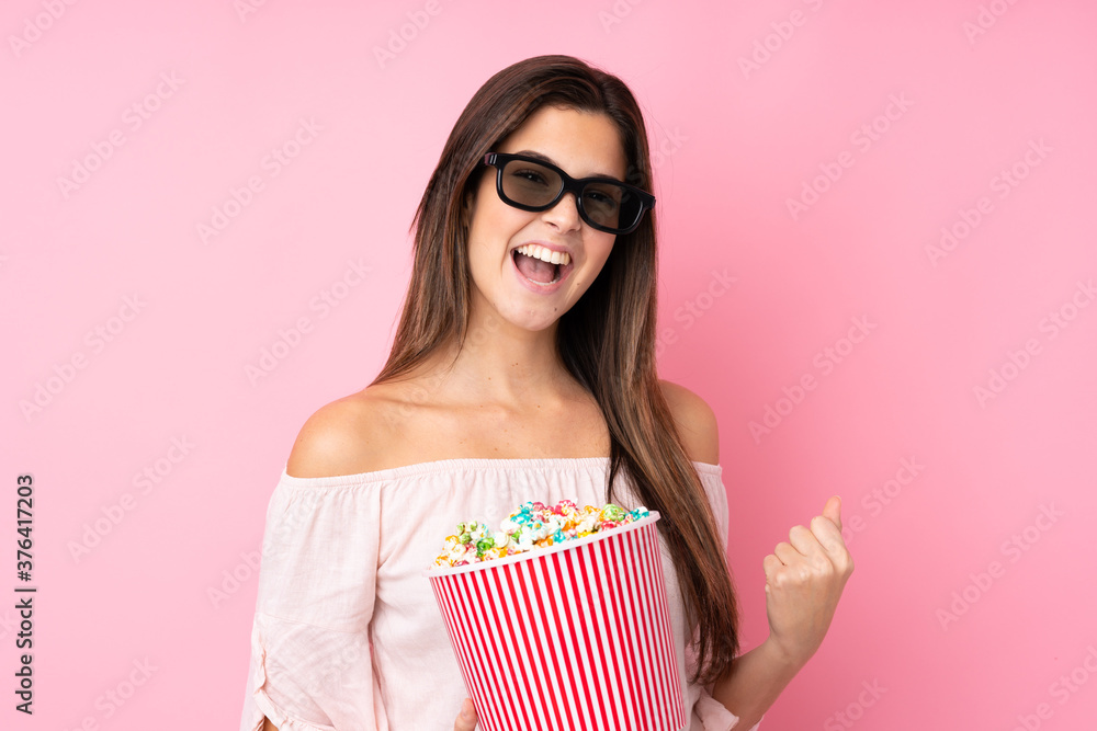 Teenager girl over isolated pink background with 3d glasses and holding a big bucket of popcorns Teenager girl over isolated pink background with 3d glasses and holding a big bucket of popcorns