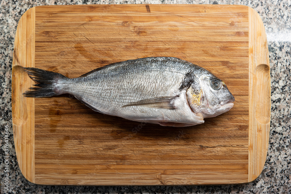 Market frozen silver sea bream raw uncooked fish top view sitting on a wooden board on a kitchen countertop Market frozen silver sea bream raw uncooked fish top view sitting on a wooden board on a kitchen countertop