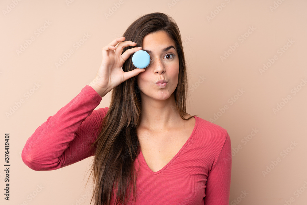 Teenager girl over isolated background holding colorful French macarons with funny face Teenager girl over isolated background holding colorful French macarons with funny face