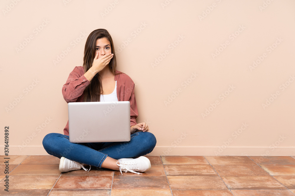 Teenager student girl sitting on the floor with a laptop covering mouth with hands Teenager student girl sitting on the floor with a laptop covering mouth with hands