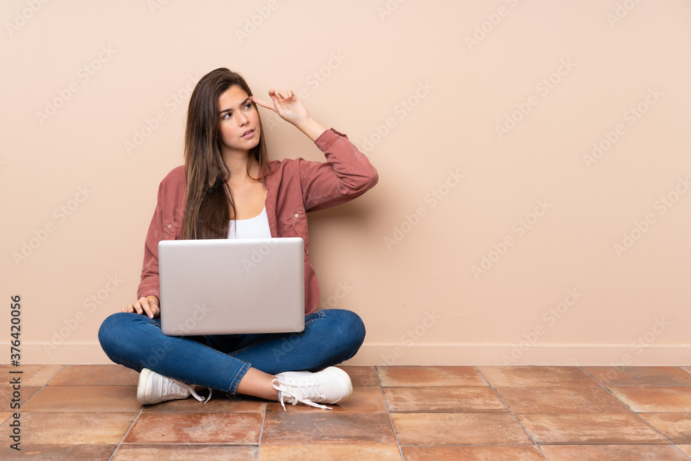 Teenager student girl sitting on the floor with a laptop making the gesture of madness putting finger on the head Teenager student girl sitting on the floor with a laptop making the gesture of madness putting finger on the head