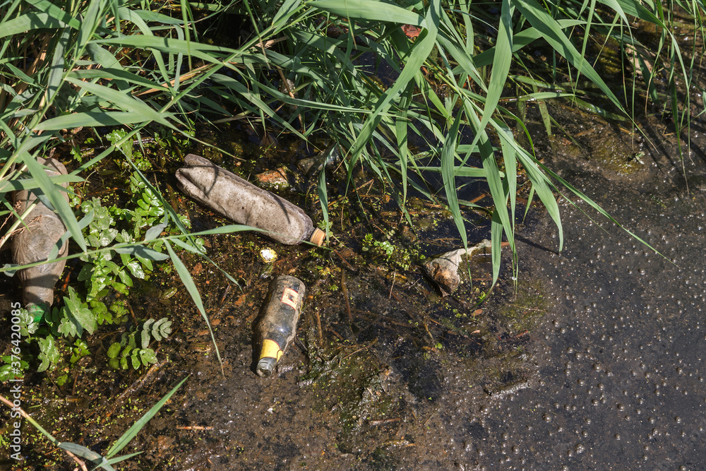 Spilled garbage to small river. Empty used dirty plastic bottles float in canal water. Pollution of environment by household waste. Ecological problem. River contaminated with various garbage Spilled garbage to small river. Empty used dirty plastic bottles float in canal water. Pollution of environment by household waste. Ecological problem. River contaminated with various garbage