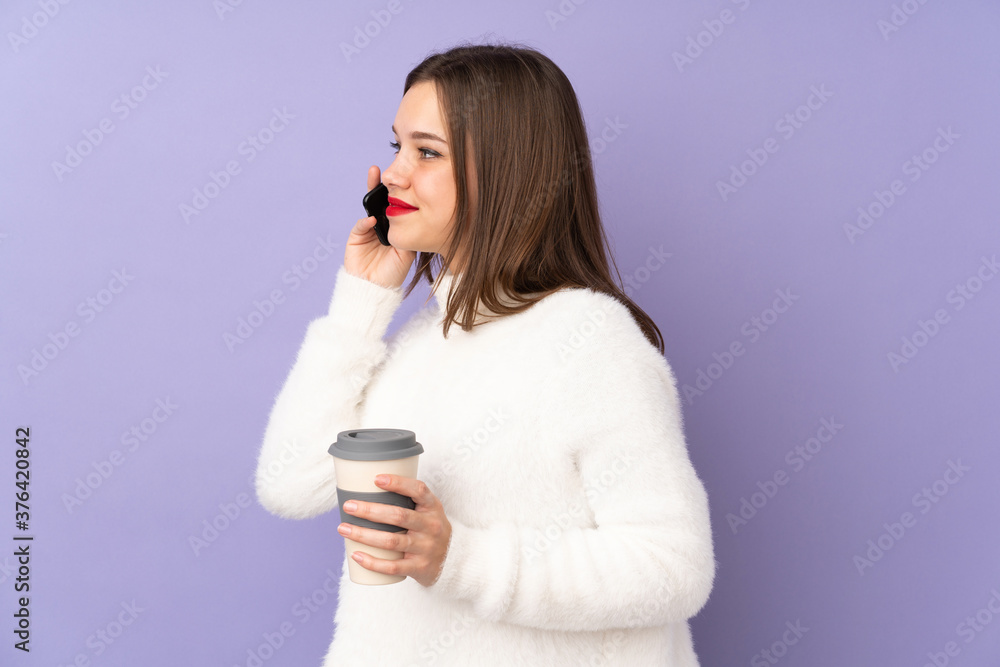 Teenager girl isolated on purple background holding coffee to take away and a mobile Teenager girl isolated on purple background holding coffee to take away and a mobile