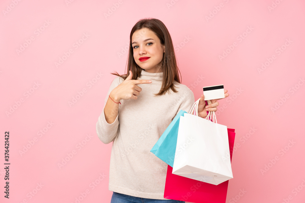 Teenager girl isolated on pink background holding shopping bags and a credit card Teenager girl isolated on pink background holding shopping bags and a credit card