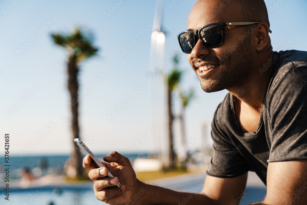 Image of smiling african american man using cellphone while sitting