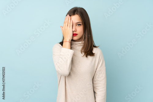 Teenager girl isolated on blue background covering a eye by hand