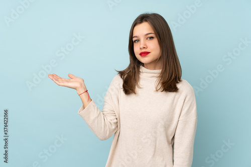 Teenager girl isolated on blue background holding copyspace imaginary on the palm