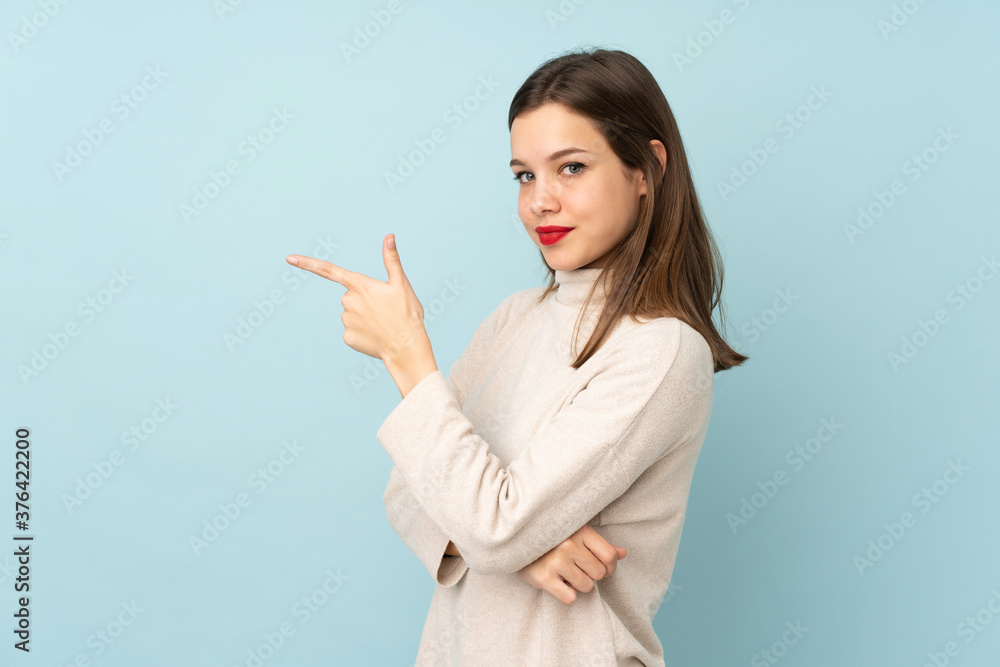 Teenager girl isolated on blue background pointing finger to the side Teenager girl isolated on blue background pointing finger to the side
