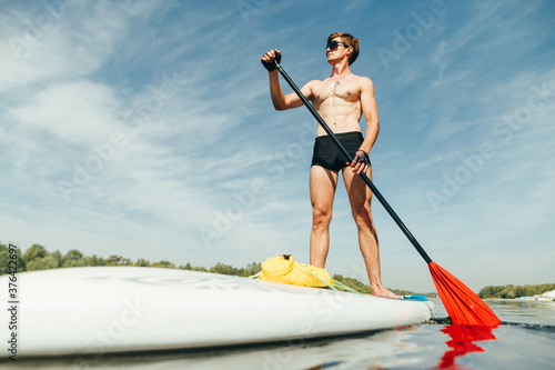 Athletic young man paddles on a sup board on the river. Training on a rowing board. Active recreation on the water.