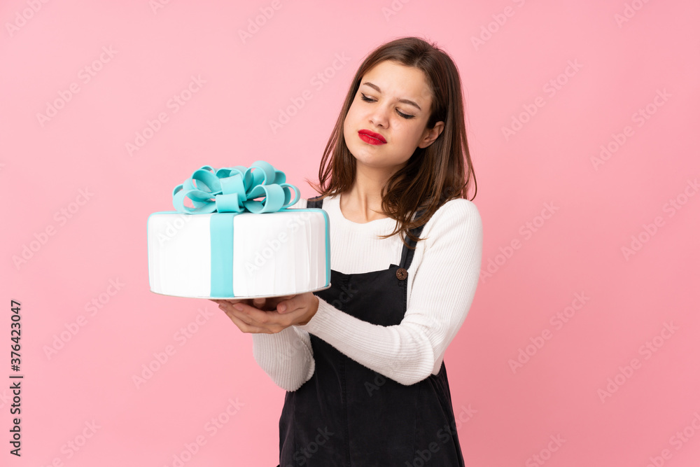 Girl holding a big cake isolated on pink background with sad expression Girl holding a big cake isolated on pink background with sad expression