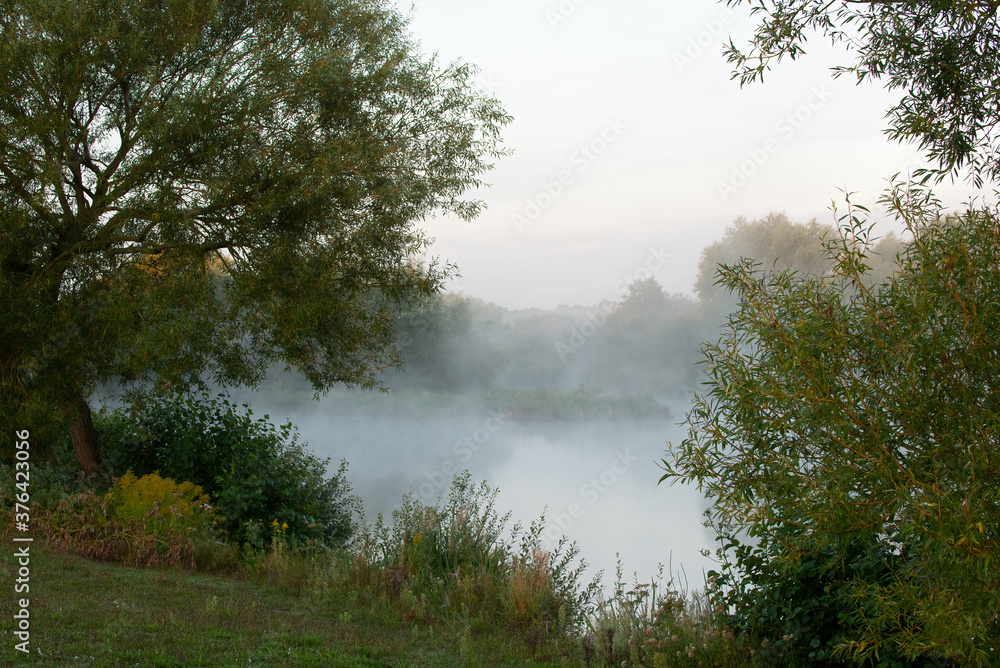 Peaceful early morning mist rolling over quiet lake.