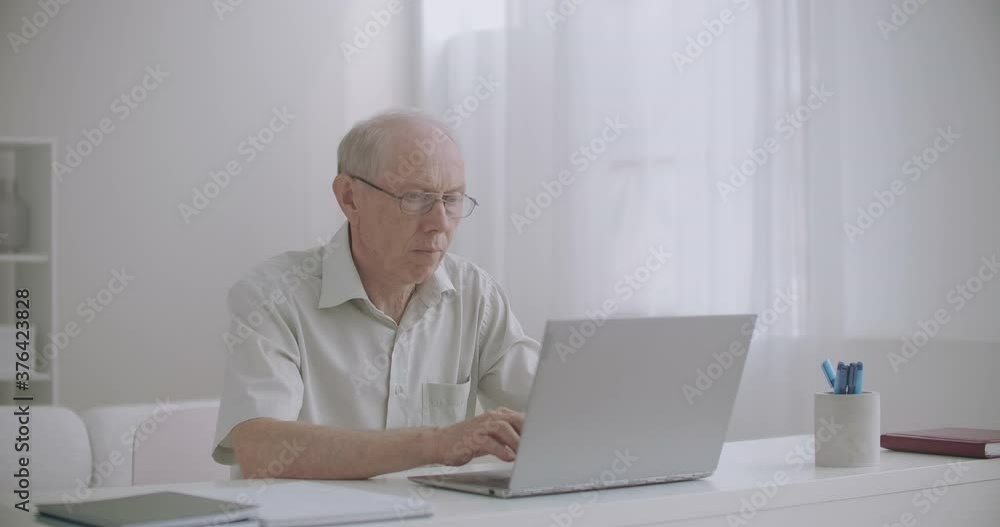 elderly male freelancer is working from home with laptop, aged writer is writing book, typing text on keyboard elderly male freelancer is working from home with laptop, aged writer is writing book, typing text on keyboard