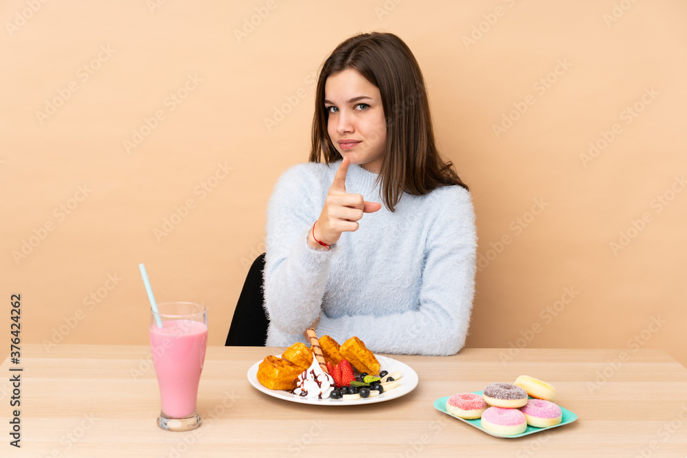 Teenager girl eating waffles isolated on beige background frustrated and pointing to the front Teenager girl eating waffles isolated on beige background frustrated and pointing to the front
