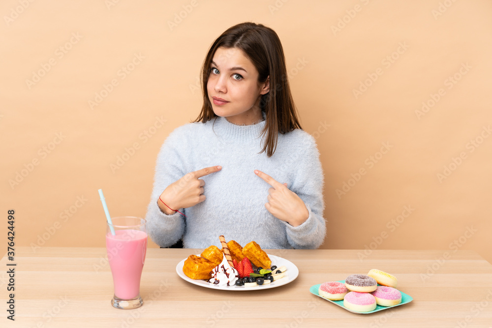 Teenager girl eating waffles isolated on beige background pointing to oneself Teenager girl eating waffles isolated on beige background pointing to oneself