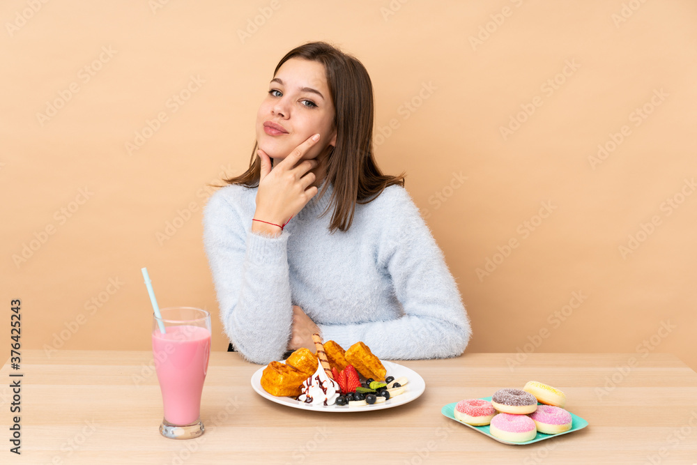 Teenager girl eating waffles isolated on beige background smiling Teenager girl eating waffles isolated on beige background smiling